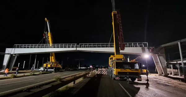 Dos grúas colocando de noche un puente peatonal sobre una carretera