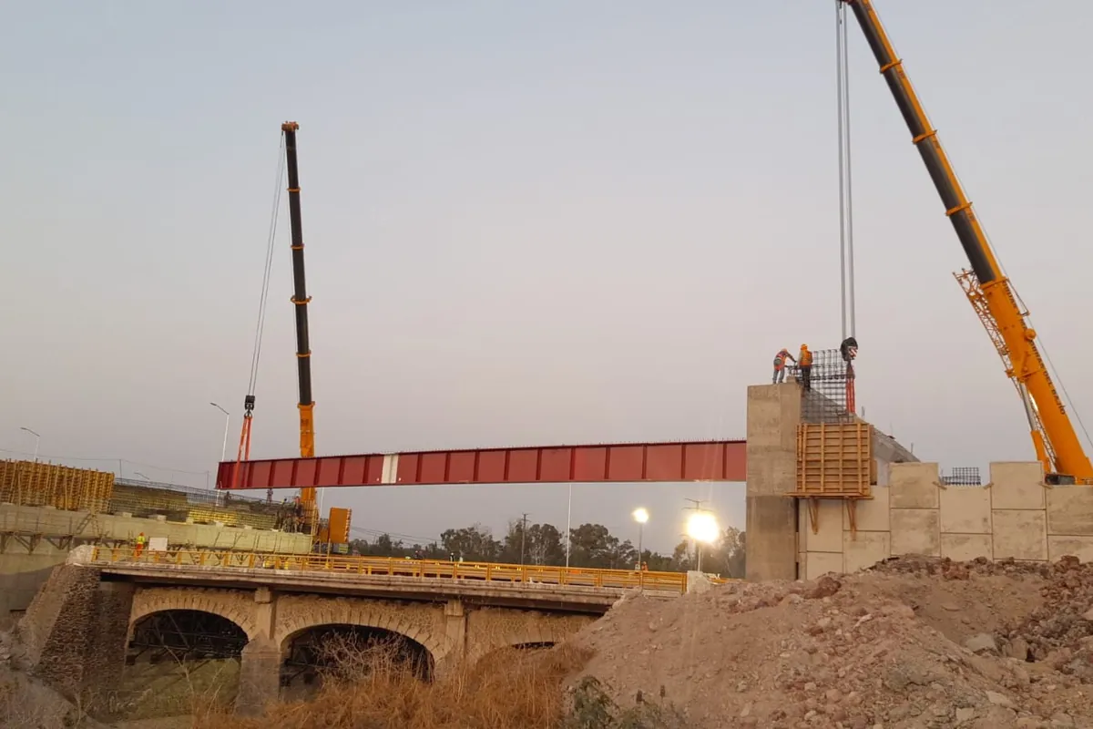 Dos grúas colocando una trabe de acero sobre las pilas de un puente