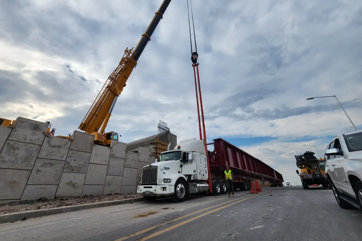 Grúa izando una trabe de acero desde la plataforma de un camión